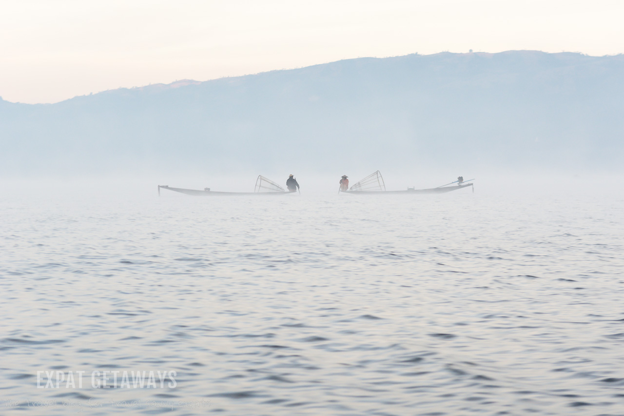 Fishermen sit and talk on their small boats early in the morning, surrouned by morning fog on Inle Lake, Myanmar. 
